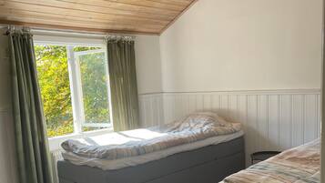 A room with a wooden ceiling, a window with curtains, a bed, and a bench.