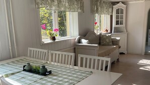 Een kamer met een eettafel, stoelen, een bank en een raam met gordijnen.