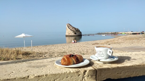 A beach scene with a pastry and a cup of coffee on a concrete ledge. - Casa Vacanze Marello - A 400 M Dalla Spiaggia (Salve)