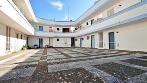 A spacious courtyard with a checkered floor pattern, surrounded by white buildings with blue accents and multiple doors. - Casa Vacanze Marello - A 400 M Dalla Spiaggia (Salve)