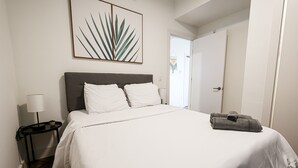 A neatly made bed with white linens, a gray headboard, and a single pillow. A gray towel is placed on the bed.