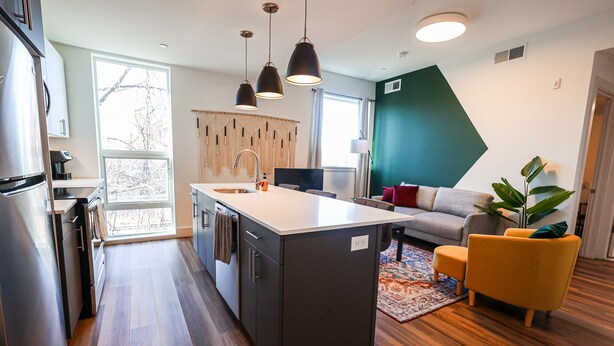 A modern kitchen with a central island, a dining area with a sofa, and a living room with a plant.
