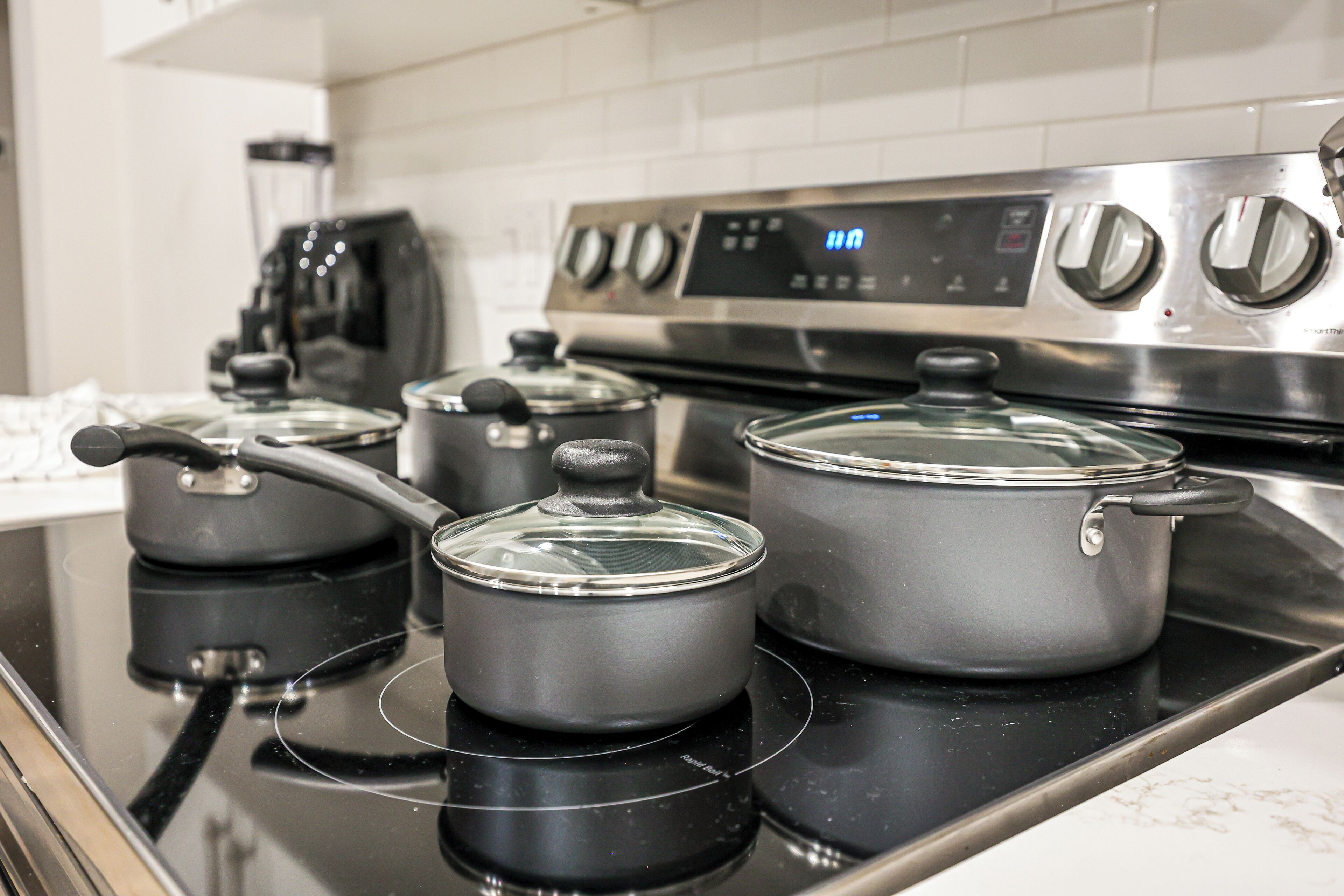 A kitchen with a stainless steel stove, three pots on the burners, and a digital clock displaying the time.