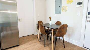 A modern kitchen with a stainless steel refrigerator, a wooden dining table with four chairs, and a vase with dried plants on the wall.