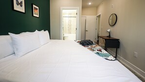 Un letto rifatto con lenzuola bianche, un comodino con una lampada e due quadri appesi al muro.