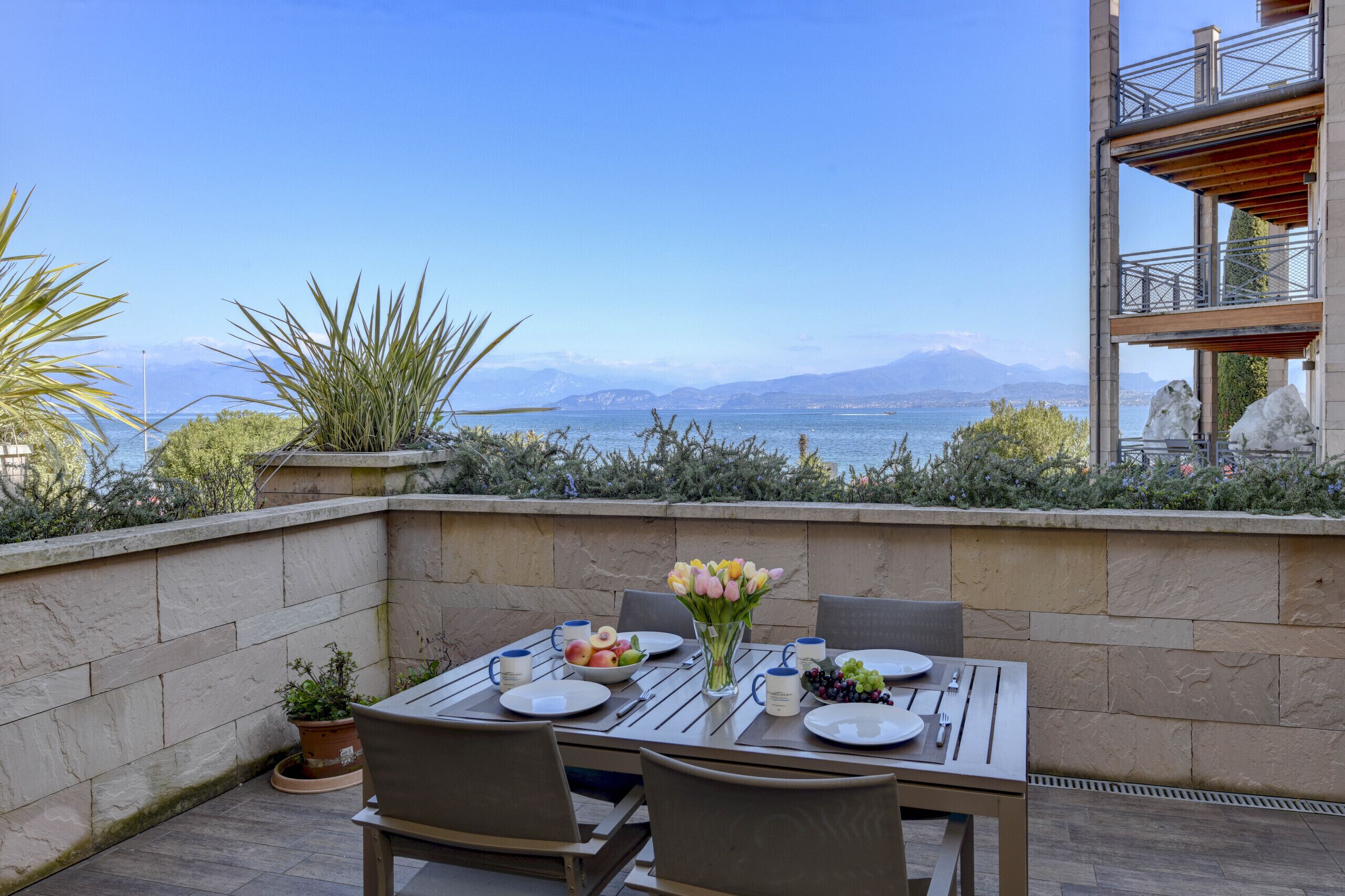 Eine Terrasse mit Esstisch und Blick auf eine malerische Berg- und Wasserlandschaft.