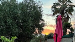 A wooden outdoor table with four chairs, a pink umbrella, and a sunset in the background. - LA MAISON DU SOLEIL MAGNIFICENT NEW EQUIPPED T3 IN PORTICCIO (Grosseto-Prugna)