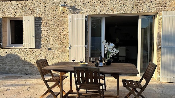 An outdoor dining area with a stone wall, wooden table, and chairs. - LA MAISON DU SOLEIL MAGNIFICENT NEW EQUIPPED T3 IN PORTICCIO (Grosseto-Prugna)
