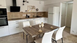 A modern kitchen with white cabinetry, a wooden dining table, and a built-in oven. - LA MAISON DU SOLEIL MAGNIFICENT NEW EQUIPPED T3 IN PORTICCIO (Grosseto-Prugna)