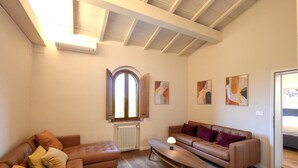 Een ruime woonkamer met een hoge plafond, een groot rondboogvenster en een open haard.