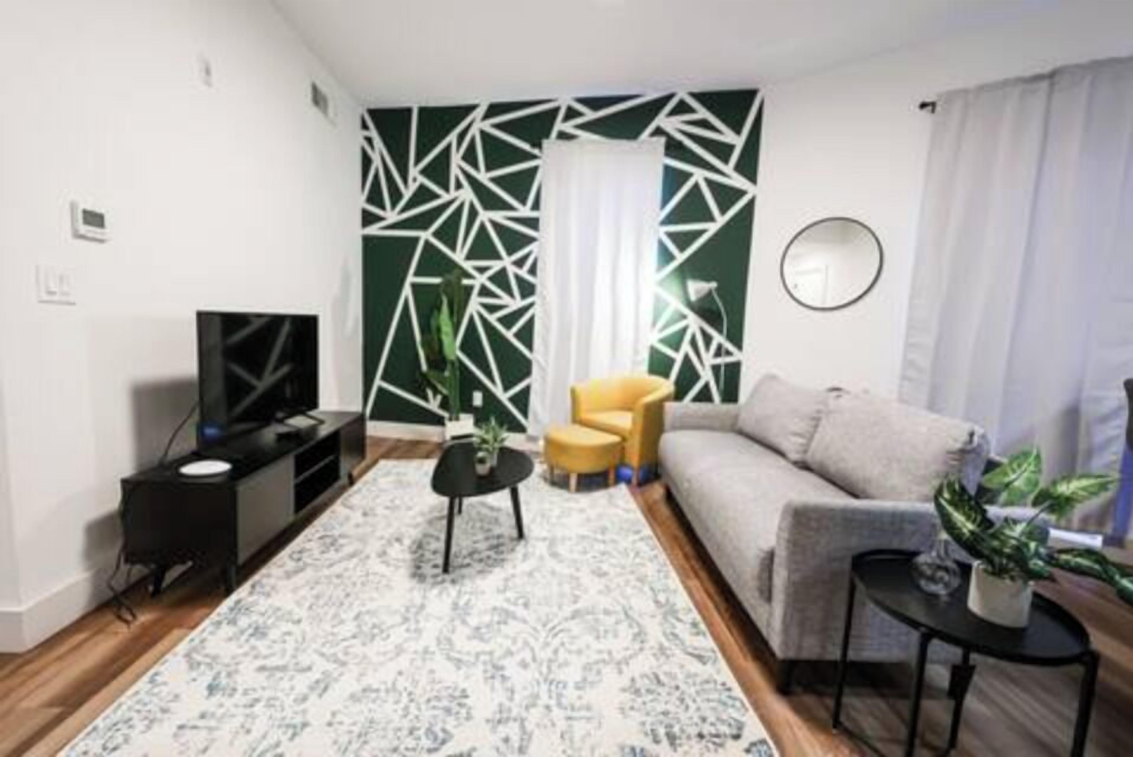 Ein modernes Wohnzimmer mit einer Couch, einem gelben Sessel, einem schwarzen Couchtisch und einem Fernseher auf einem schwarzen Schrank.