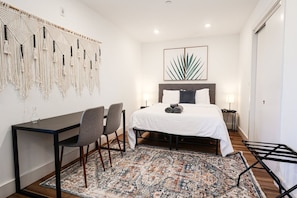 Une chambre à coucher comprenant un lit, un bureau, deux chaises, un tapis à motifs et une décoration murale en macramé.