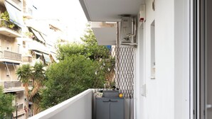 Varanda com mesa e cadeiras, pequena cozinha e vista para edifícios próximos.