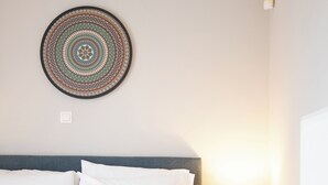 Uma cama bem arrumada com almofadas listradas em branco e azul, um ornamento circular na parede e uma mesa de cabeceira com uma luminária.
