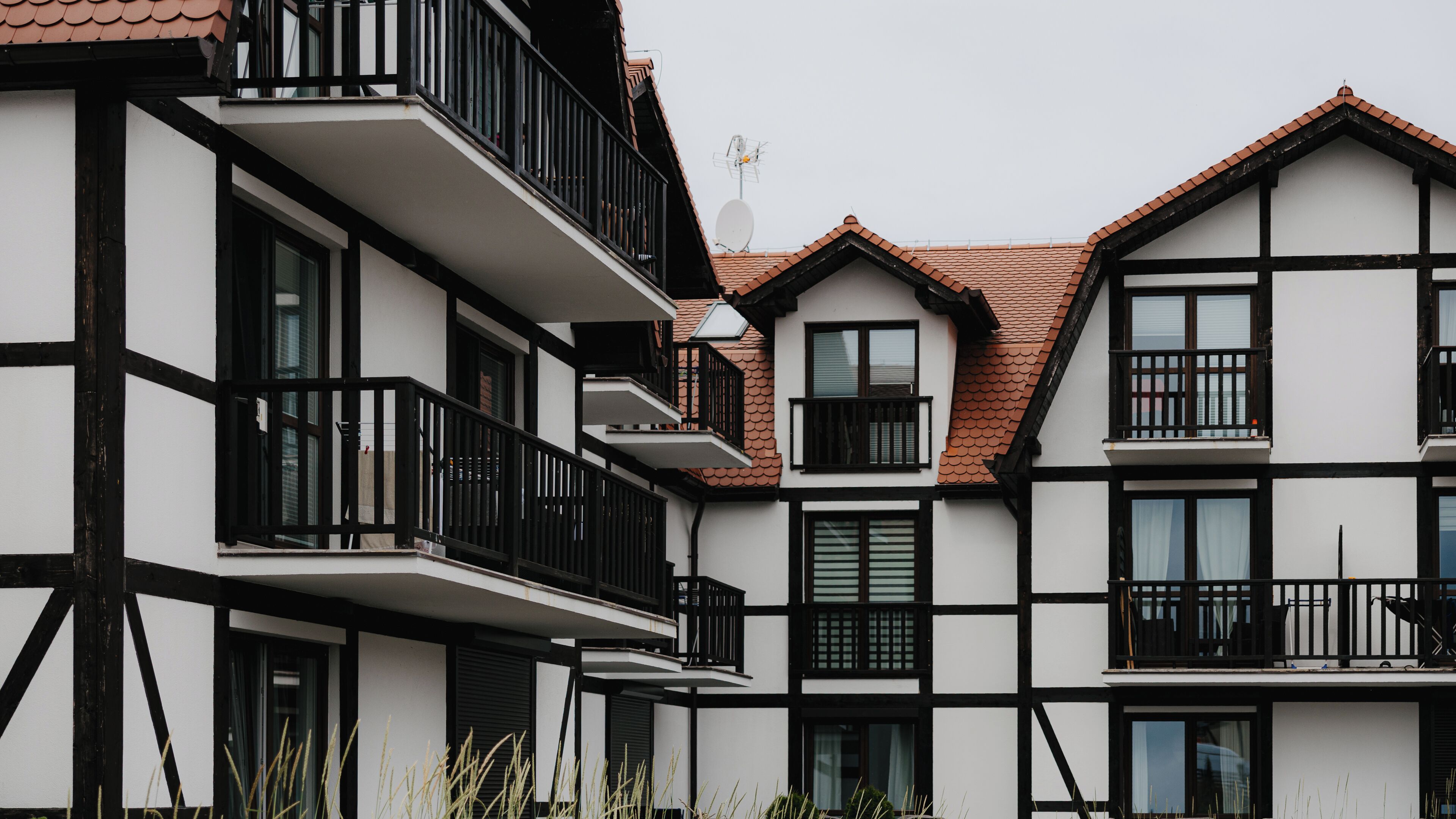 A modern multi-story building with black railings and white walls, featuring balconies and large windows.