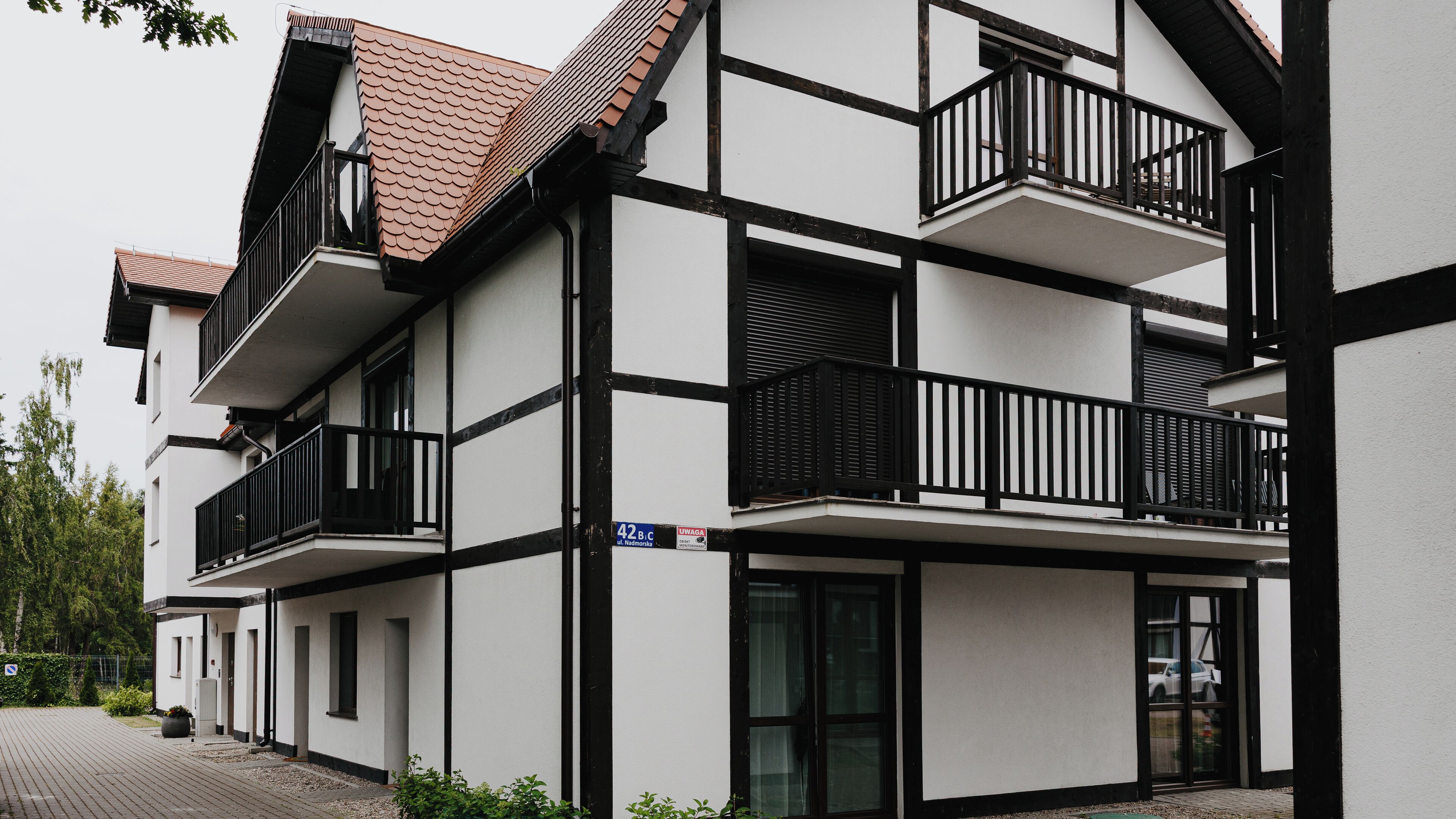 Un edificio moderno con fachada blanca, detalles negros y varios balcones con barandillas negras.