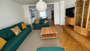 A living room with a green sofa set, a wooden coffee table, a TV cabinet, and a hanging light fixture. - Large apartment in the center of Plön within walking distance to the lake/shops. Children's room (Plön)