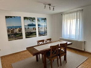 A dining area with a wooden table and chairs, three framed pictures on the wall, a window with sheer curtains, and a radiator. - Large apartment in the center of Plön within walking distance to the lake/shops. Children's room (Plön)