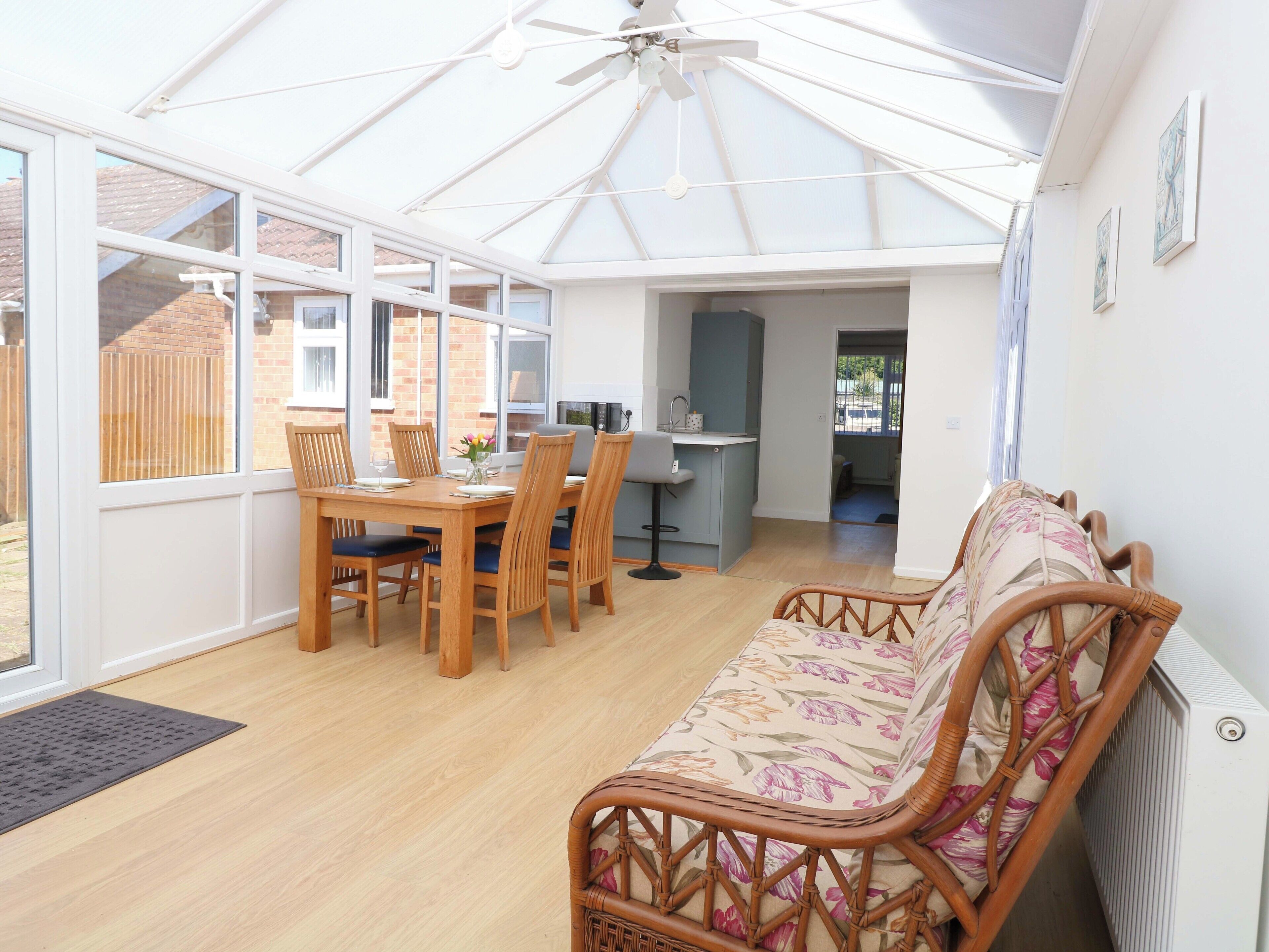 A conservatory with a dining area, a kitchen, and a seating area with a sofa.