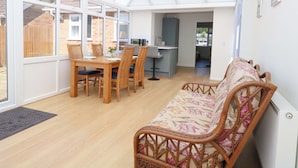 A conservatory with a dining area, a kitchen, and a seating area with a sofa. - Bankside Cottage (King's Lynn)