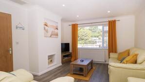 A living room with a sofa, a coffee table, a TV, and a window with curtains. - Bankside Cottage (King's Lynn)