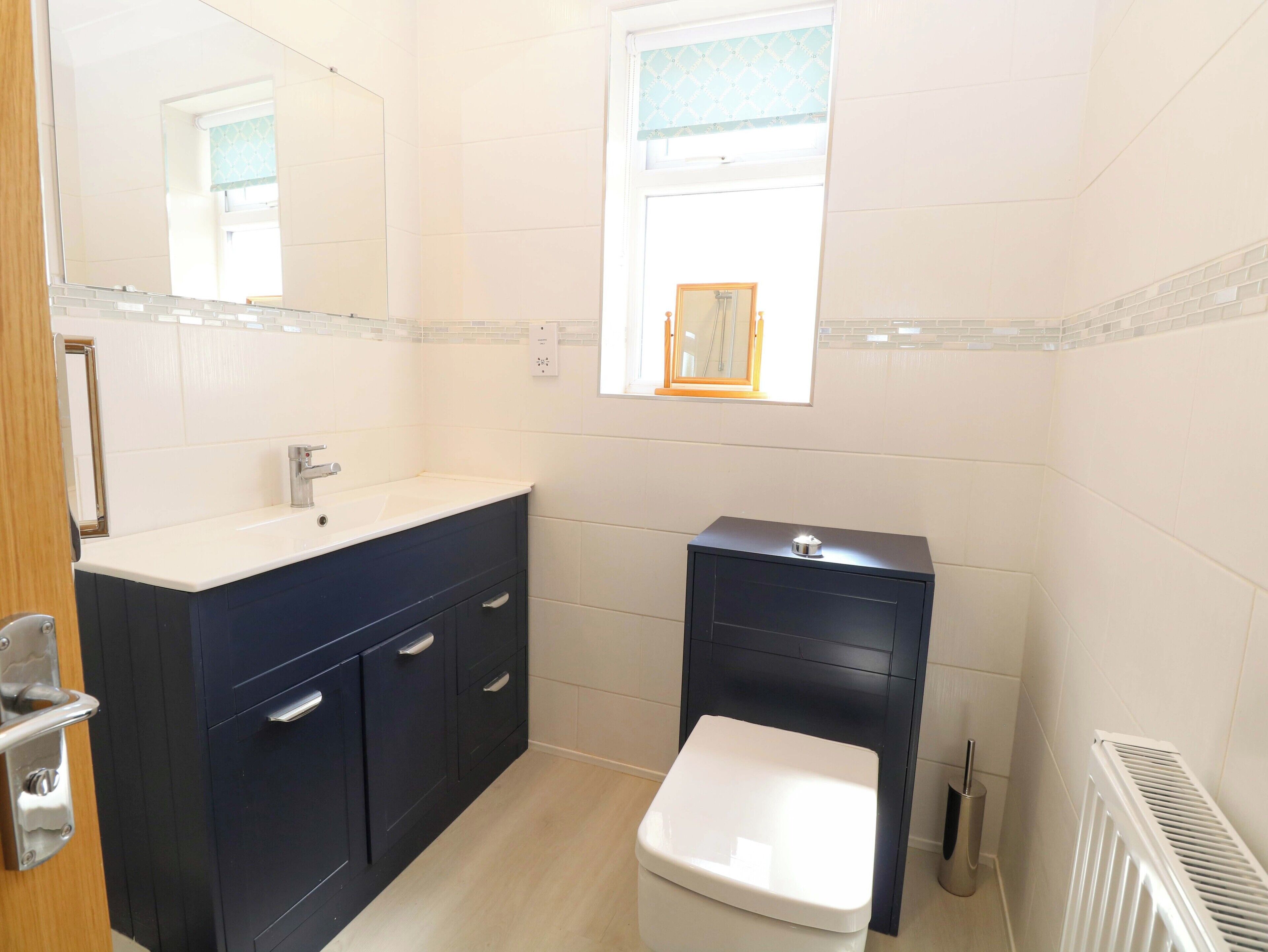 A bathroom with a white sink, dark cabinets, a white toilet, and a window with a mirror.