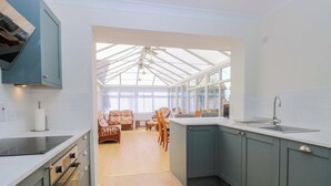 A modern kitchen with a large island, built-in appliances, and a view through a glass ceiling to a dining area. - Bankside Cottage (King's Lynn)