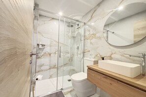 A modern bathroom with a glass-enclosed shower, a white toilet, a wooden vanity, and a marble backsplash.