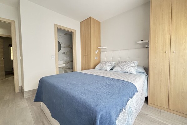 A bedroom with a bed, wooden wardrobe, and a door with a marble wall.