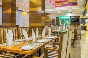 Un restaurante con mesas y sillas de madera, impecablemente dispuesto con platos, vasos y cubiertos.