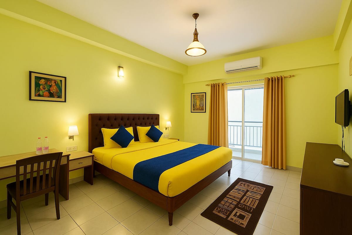 Habitación de hotel con cama, escritorio, silla, aire acondicionado, televisor y balcón con cortinas.