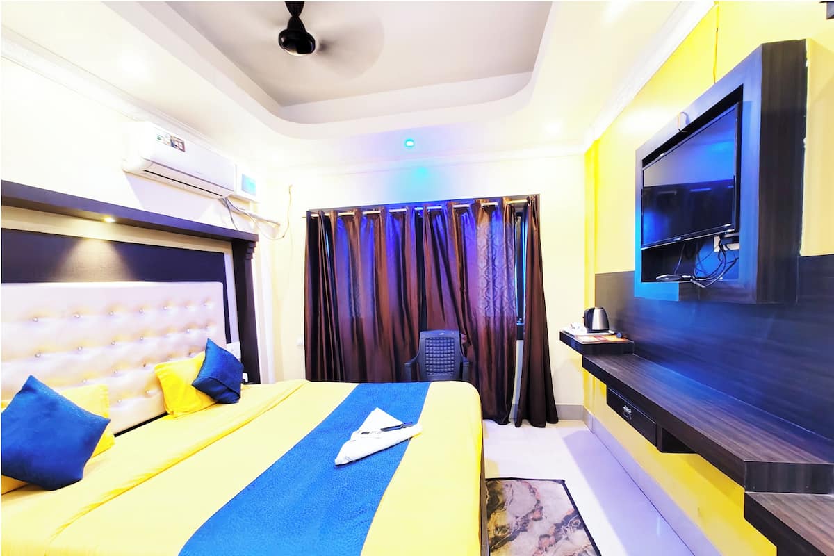 Habitación de hotel con cama, televisor de pantalla plana, escritorio con silla y ventilador de techo.
