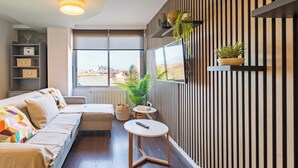 A modern living room with a sofa, a small table, and a TV mounted on a striped wall. - 🌿✨ Calm, light and design in the center of Santander 🏙️🛋️ (Santander)