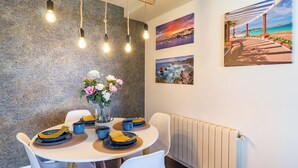A dining area with a round table, white chairs, and a vase with flowers. There are light fixtures above the table and a radiator below it. - 🌿✨ Calm, light and design in the center of Santander 🏙️🛋️ (Santander)
