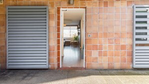 A building entrance with a tiled wall, a closed grey shutter door, and a visible interior with a table and chairs. - 🌿✨ Calm, light and design in the center of Santander 🏙️🛋️ (Santander)