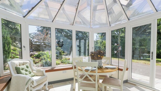 A conservatory with a glass roof, white furniture, and a view of a garden. - Nithbank Cottage (Thornhill)