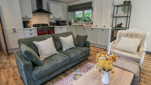 A compact living space with a kitchenette, a sofa, a chair, and a coffee table with a floral arrangement. - Nithbank Cottage (Thornhill)