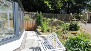 A garden with a white bench, a wooden fence, and various plants. - Nithbank Cottage (Thornhill)