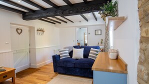 A cozy living room with a dark blue sofa, wooden coffee table, and a stone accent wall. - Little Forge  - Romantic retreat in Bourton-on-the-Water (Bourton-on-the-Water)