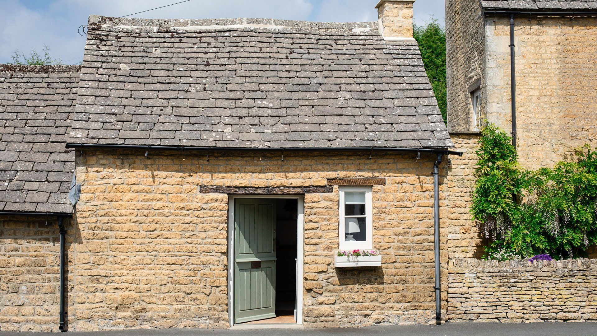 Un bâtiment en pierre doté d’un toit à deux versants de style traditionnel, d’une petite fenêtre à cadre blanc et d’une porte.