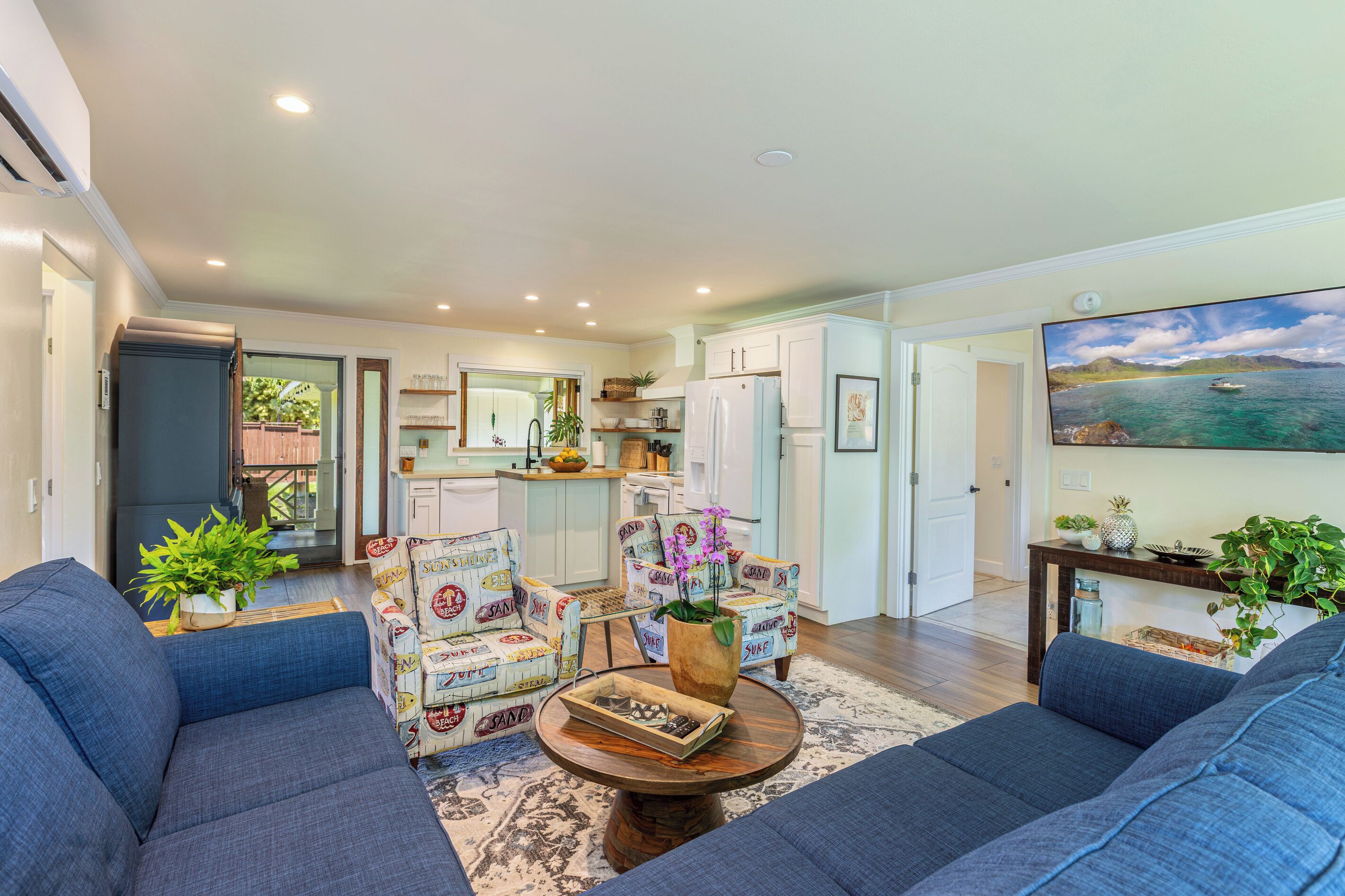 A spacious living room with a large sofa, two armchairs, a coffee table, and a view of the kitchen and dining area.