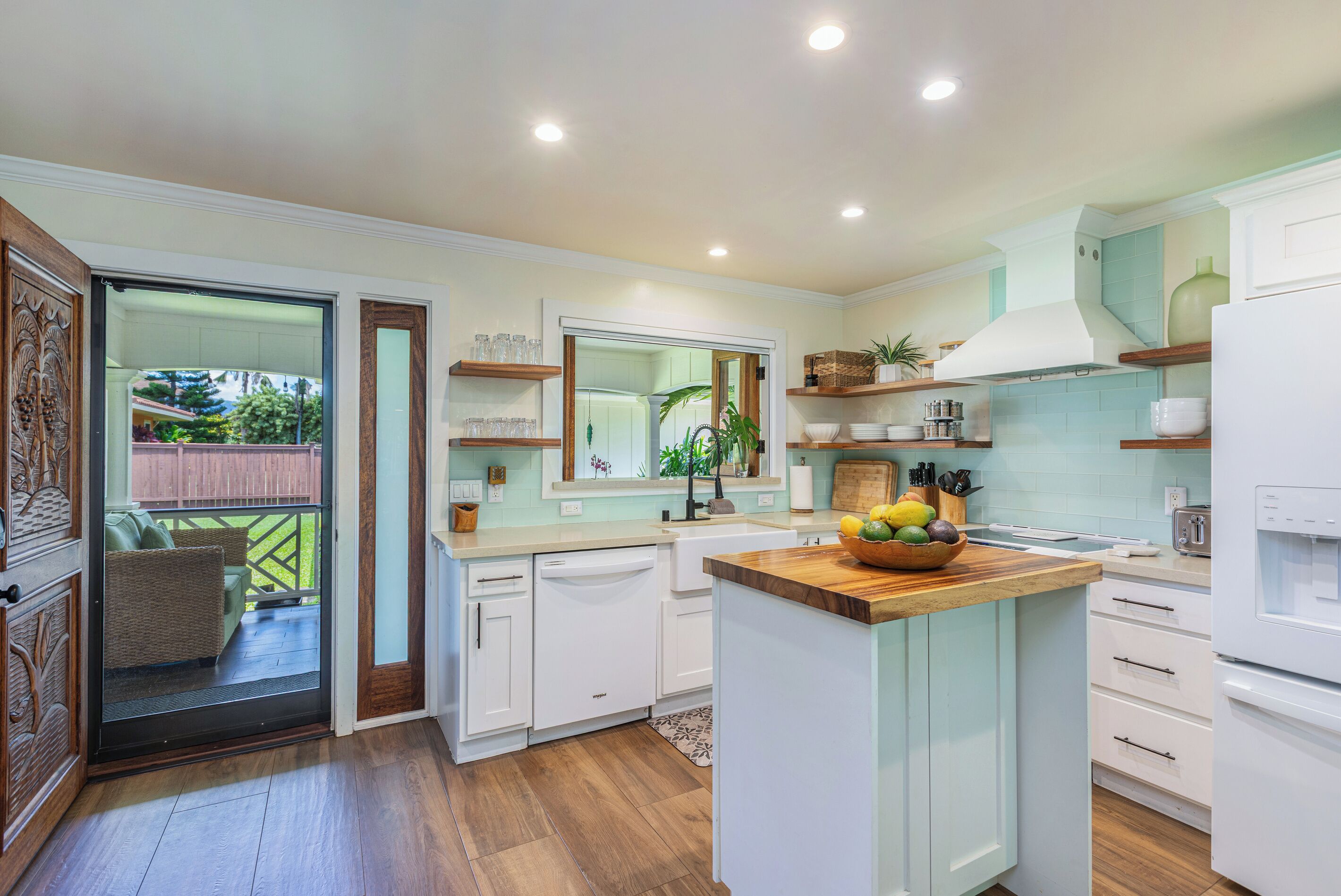 A modern kitchen with white cabinetry, a wooden island, and a view to a balcony.