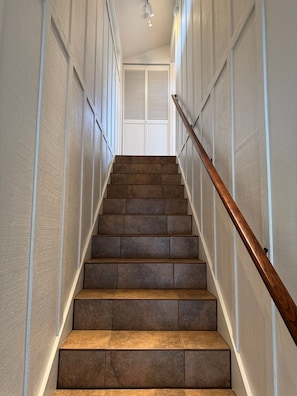 Una escalera con barandilla de madera que lleva a una puerta cerrada con persianas.