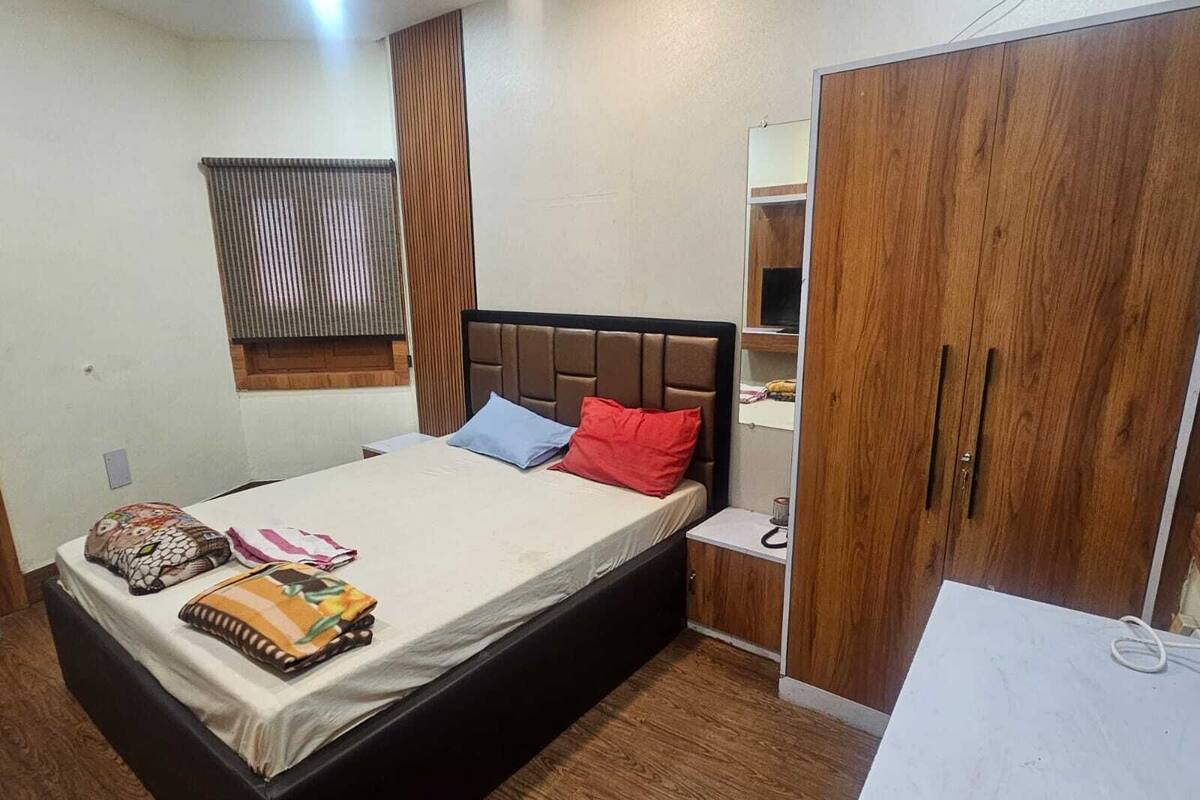 Quarto com cama, mesa de cabeceira, guarda-roupa e janela com persianas.