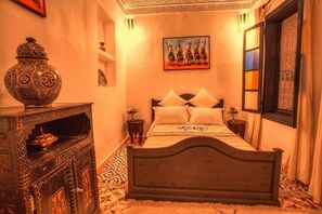 A bedroom with a bed, a decorative cabinet, a painting, and a window with patterned curtains. - Calla Lilly, Riad 111 and Spa (Marrakech)