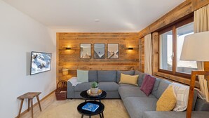 A cozy living room with a wooden accent wall, a grey sofa, a small coffee table with a book, and a window with curtains. - Apartment Diana 9 - Recently Renovated (Riddes)
