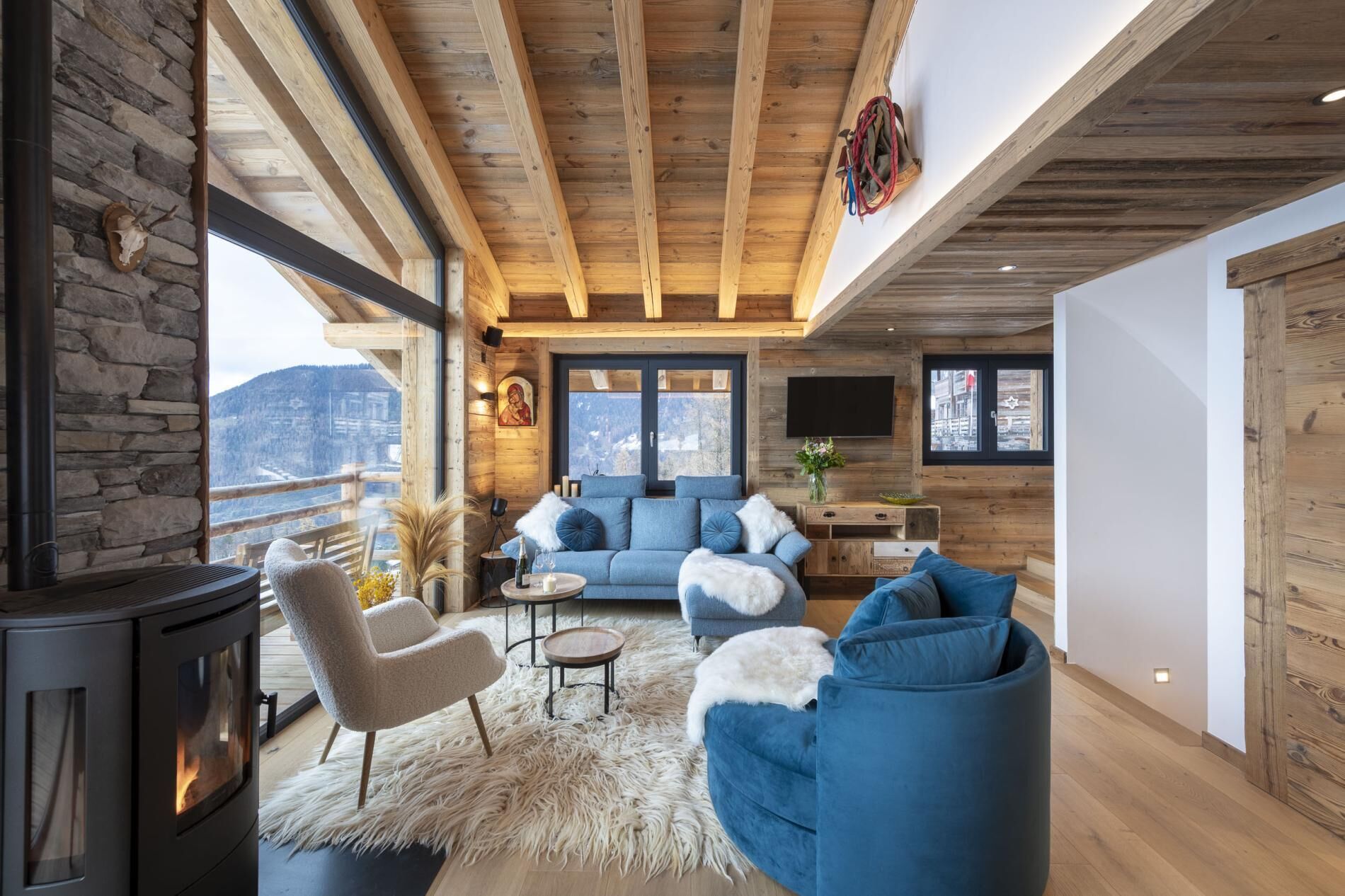 A cozy living room with a stone fireplace, a blue sofa, and a wooden ceiling.