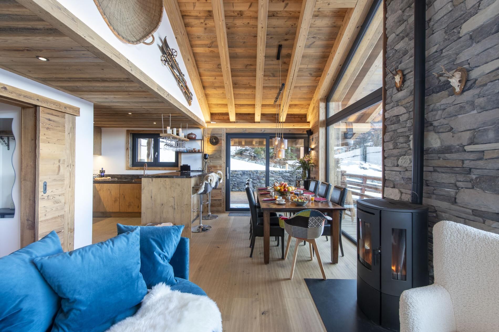 Ein gemütlicher Innenraum mit Holzbalkendecke, Steinwänden, einem Essbereich mit Tisch und Stühlen sowie einem Kamin.