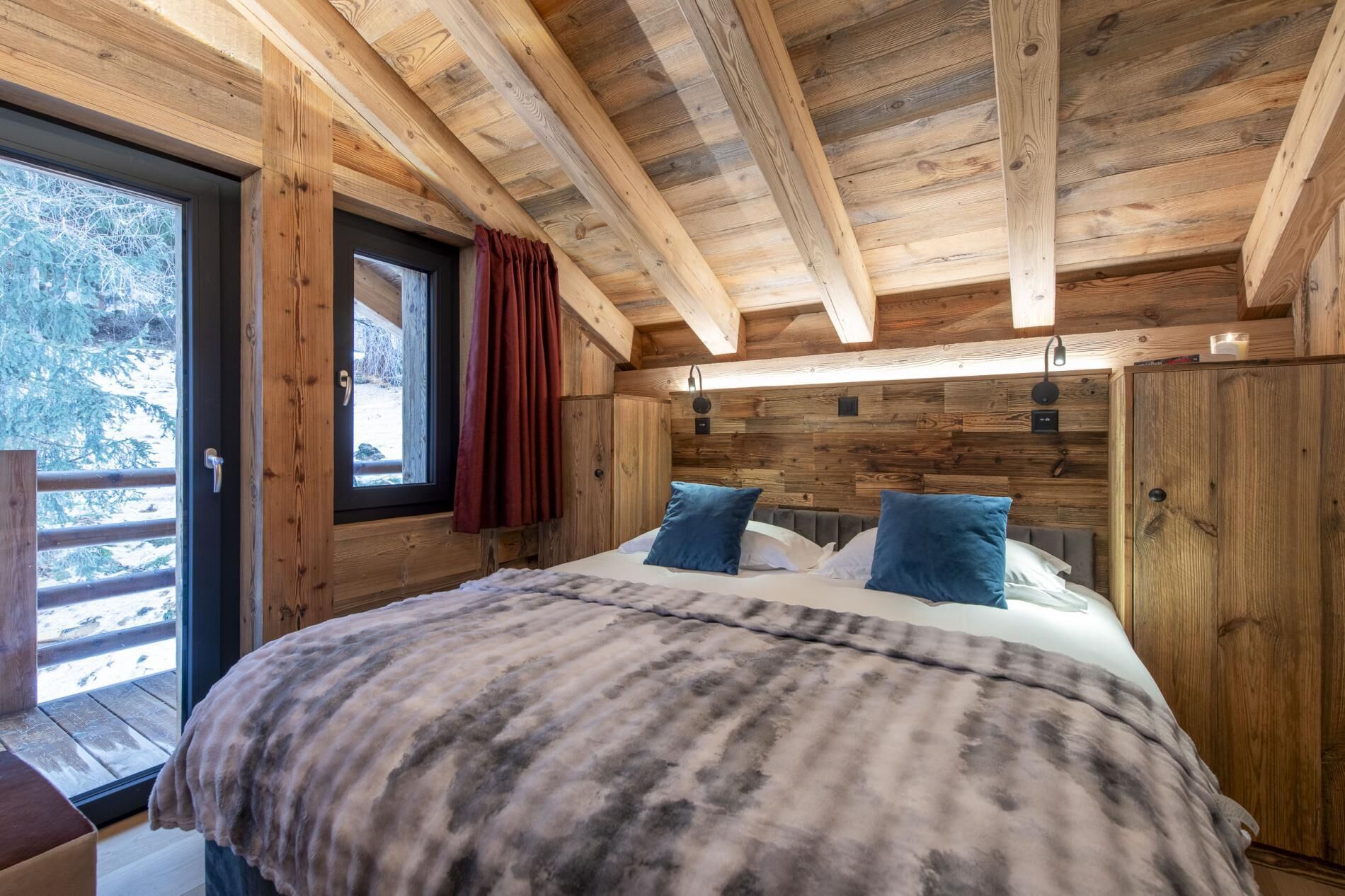 Ein Schlafzimmer einer Holzhütte mit Bett, Fenster und Tür.