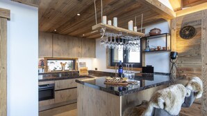Een moderne keuken met houten kasten, een centraal eiland met een zitbank bekleed met vacht, en een rustieke houten plafond.